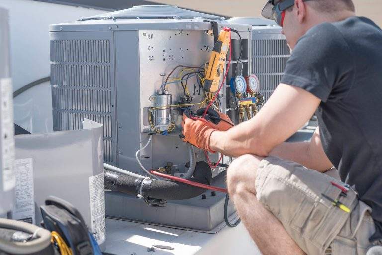 Hvac repair technician using a volt meter to test components on an air conditioner condenser.