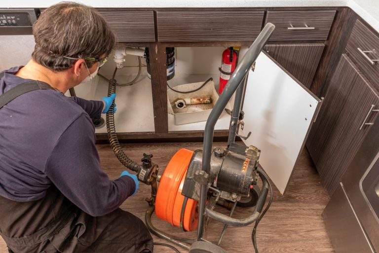 Professional plumber using an auger to clear a kitchen sink drain
